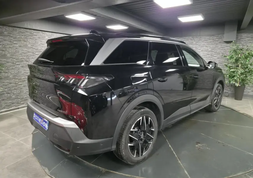 Vue 3/4 arrière droite du Peugeot 5008 noir 2025 avec jantes alliage 19'' et barres de toit noires brillantes.