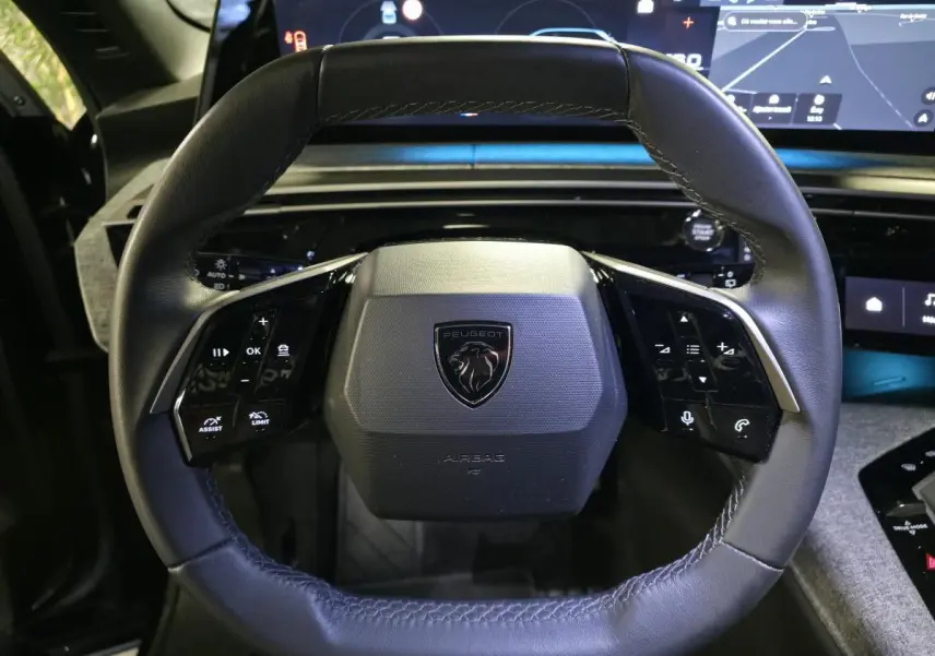 Vue rapprochée du volant compact cuir noir avec commandes intégrées et logo Peugeot sur fond intérieur moderne.
