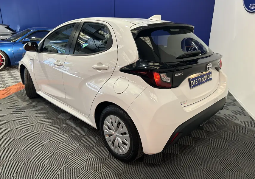 Vue 3/4 arrière droite d'une Toyota Yaris blanche avec toit noir, caméra de recul et hayon distinctif en concession.