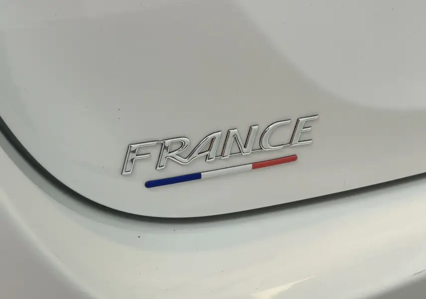 Gros plan sur l’inscription "FRANCE" avec le drapeau tricolore sur la carrosserie blanche d’une Toyota Yaris.