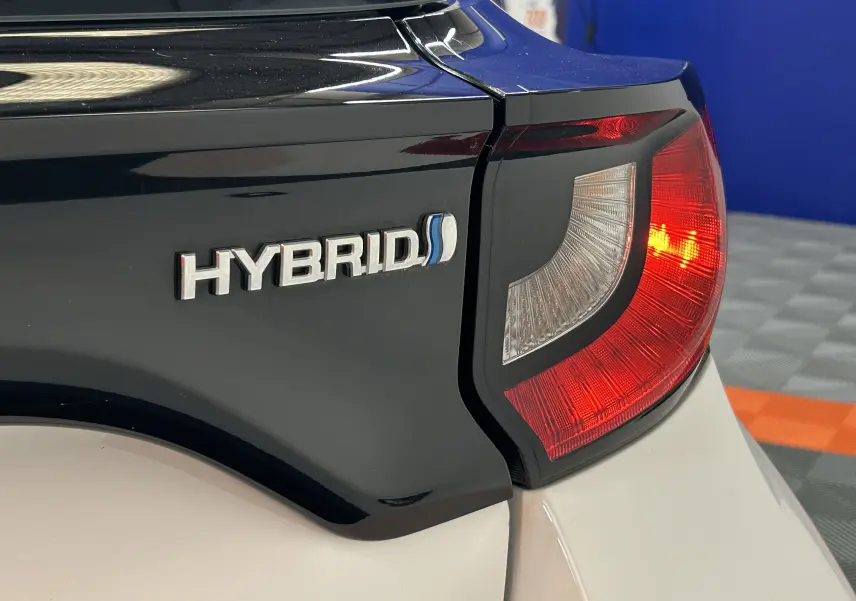 Gros plan sur le feu arrière droit et l’inscription Hybrid sur la carrosserie bicolore noir et blanc d’une Toyota Yaris.
