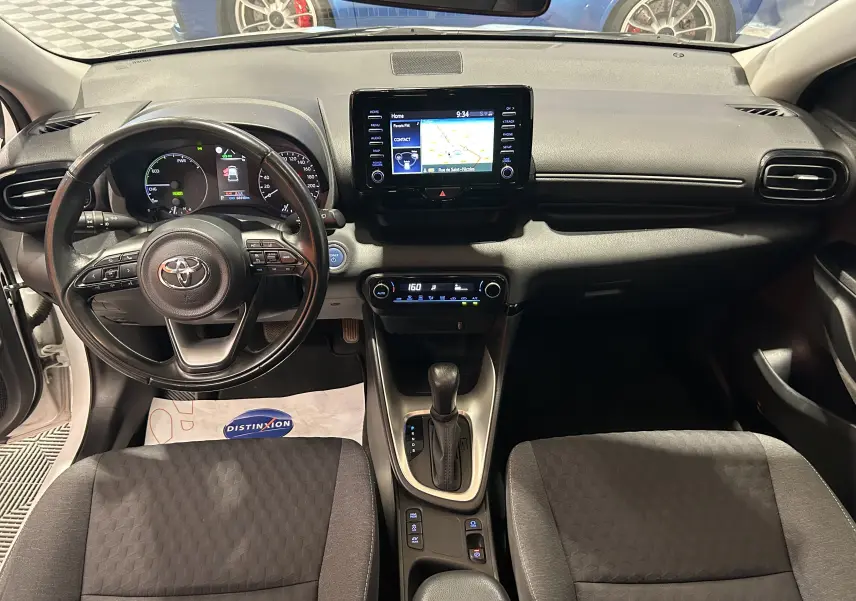 Vue intérieure de face du tableau de bord et volant noir d’une Toyota Yaris blanche avec écran GPS central allumé.