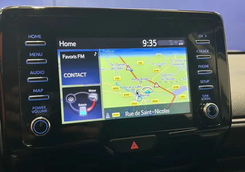 Écran tactile central de la Toyota Yaris 116h blanc montrant la navigation GPS avec carte et options audio.