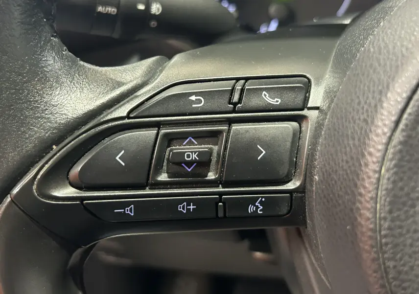 Gros plan sur les commandes multifonctions au volant côté gauche de la Toyota Yaris 116h blanche, année 2021.
