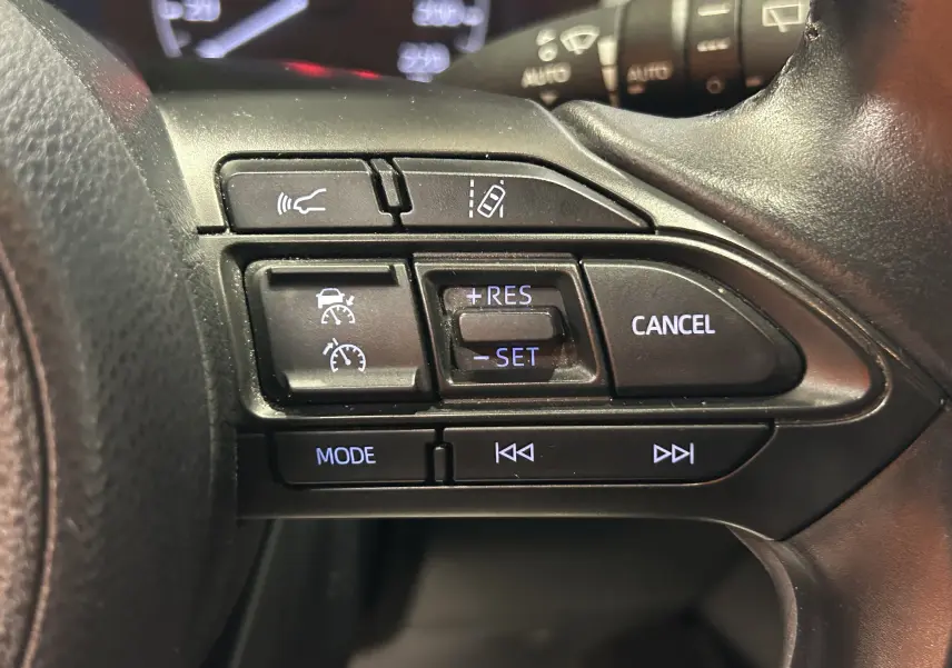 Gros plan sur les commandes au volant côté droit de la Toyota Yaris 116h blanche, avec régulateur de vitesse et mode audio.