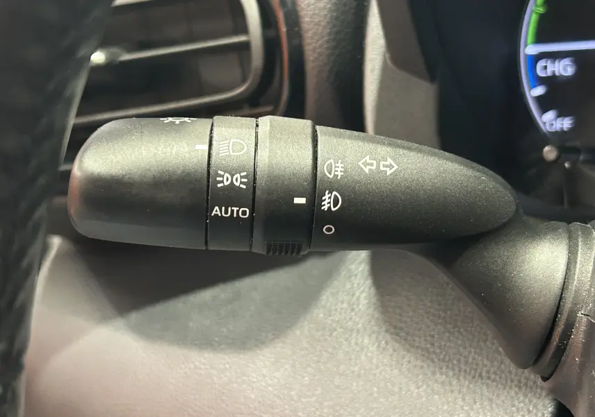Gros plan sur la commande des feux et clignotants à gauche du volant dans l’habitacle d’une Toyota Yaris blanche.