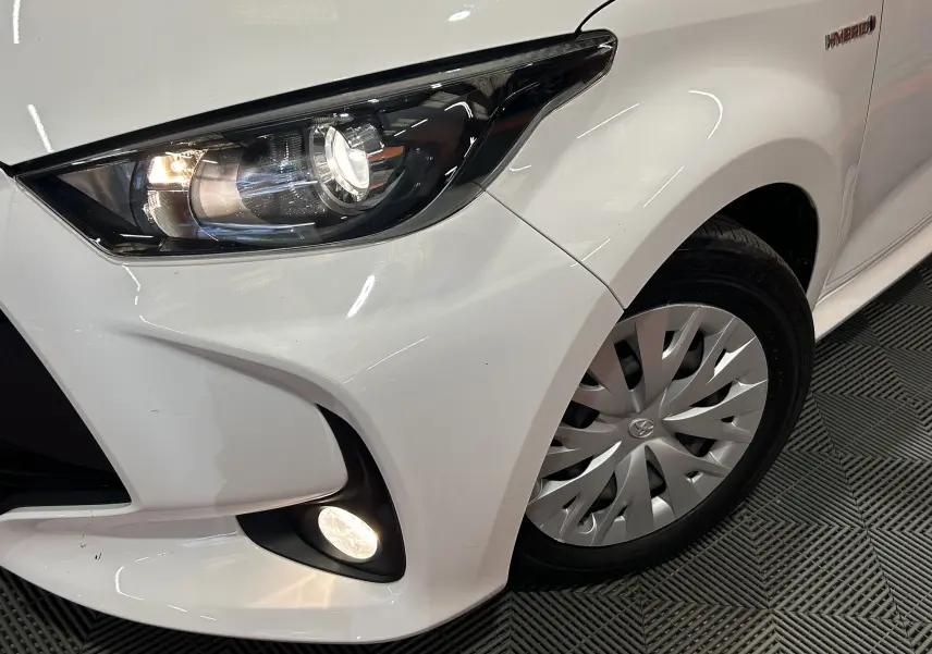 Gros plan sur l’avant droit blanc de la Toyota Yaris 116h avec phares allumés et badge Hybrid visible.