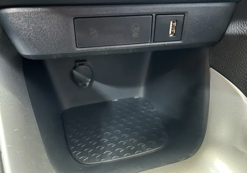 Gros plan sur la console centrale noire de la Toyota Yaris blanche, montrant une prise USB et un espace de rangement.