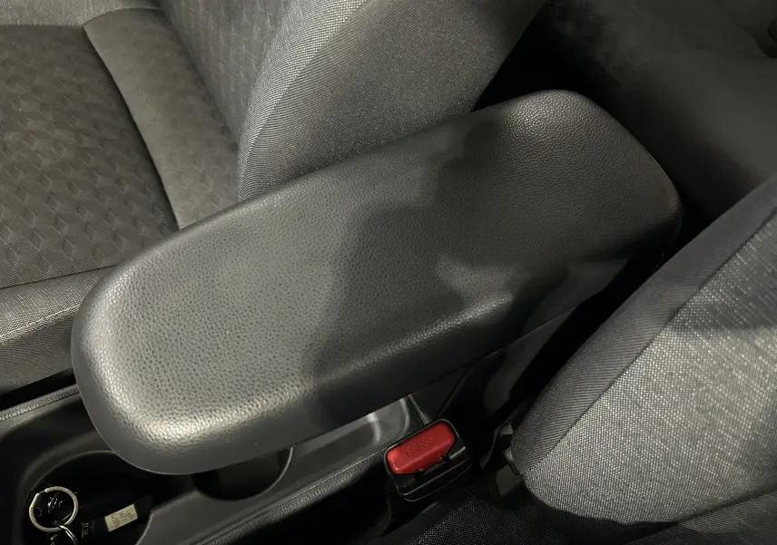 Gros plan sur l'accoudoir central noir et les sièges en tissu gris à l'intérieur de la Toyota Yaris 116h blanche.