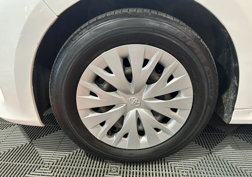 Gros plan sur la roue avant gauche blanche d'une Toyota Yaris 116h avec enjoliveur gris et logo Toyota au centre.