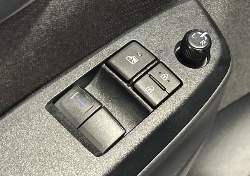 Gros plan sur les commandes de lève-vitres et réglage des rétroviseurs côté conducteur d'une Toyota Yaris blanche.