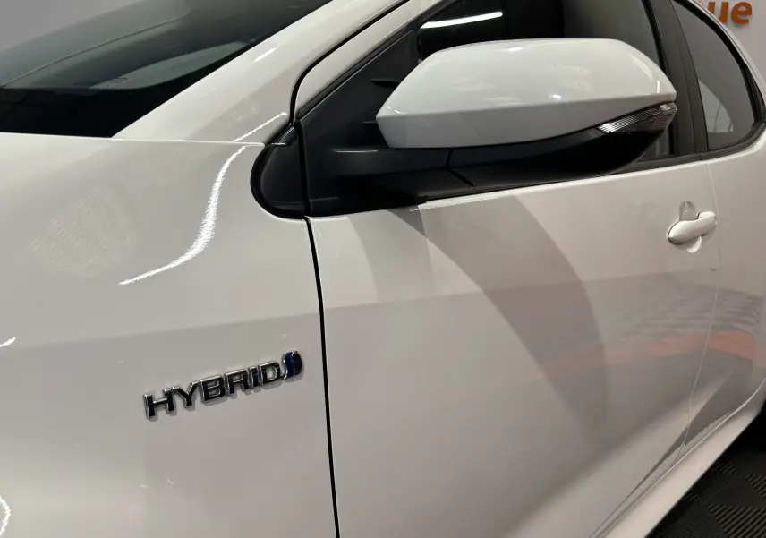 Gros plan sur la porte côté gauche d'une Toyota Yaris blanche hybride, avec rétroviseur et badge "HYBRID" visible.