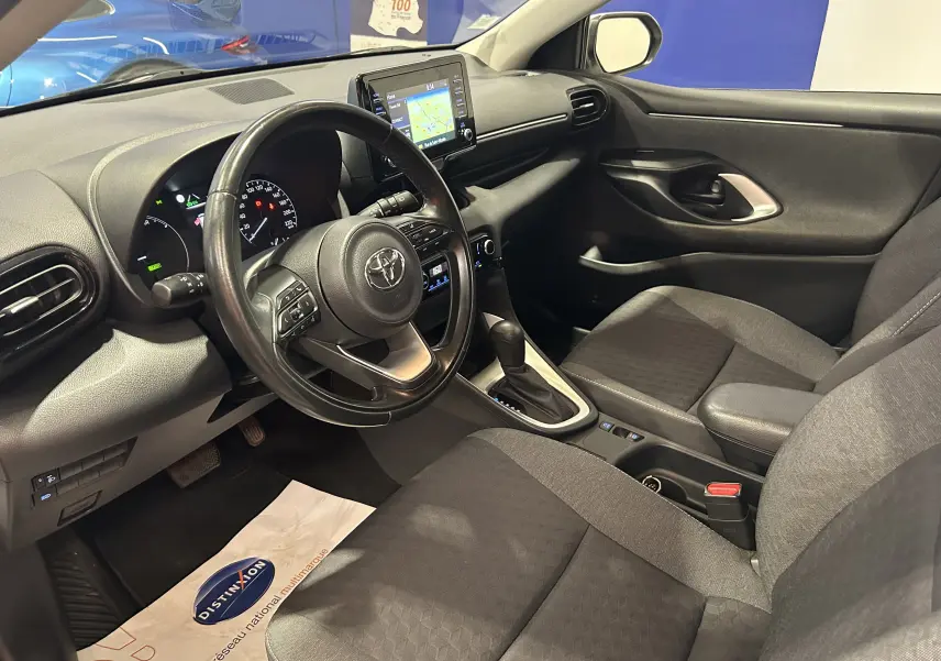 Vue intérieure côté conducteur de la Toyota Yaris 116h blanche, avec tableau de bord et écran GPS central visibles.