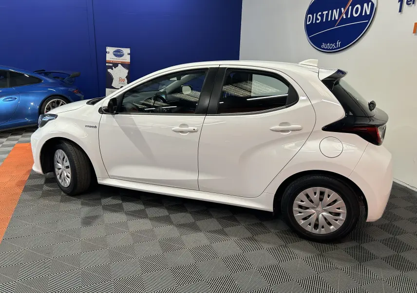 Profil côté gauche d'une Toyota Yaris hybride blanche 5 portes, en intérieur showroom avec logo Distinxion en arrière-plan.