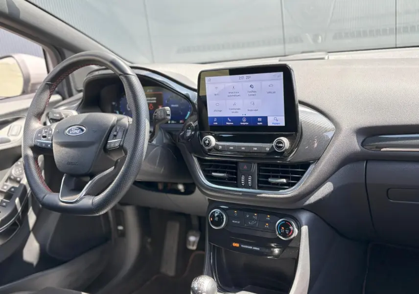 Vue intérieure avant du Ford Puma ST Line 2020, tableau de bord noir avec écran tactile central et volant sport à surpiqûres rouges.