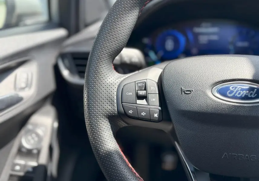 Gros plan sur le volant perforé avec surpiqûres rouges et commandes intégrées du Ford Puma Gris Solar 2020.