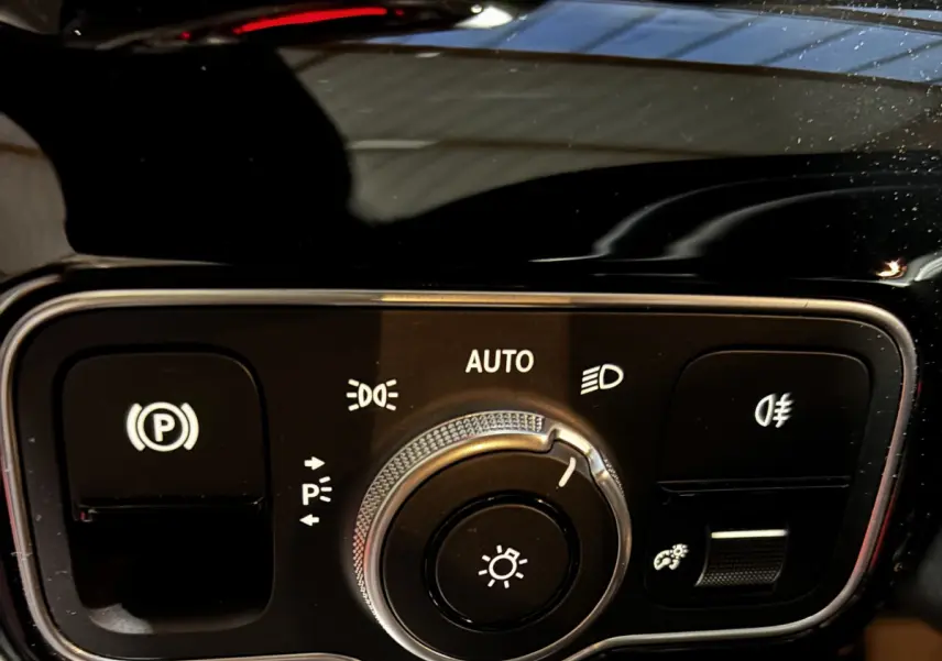 Gros plan sur la commande des phares et du frein à main électrique dans l’habitacle noir d’une Mercedes CLA 250 e AMG Line blanche.