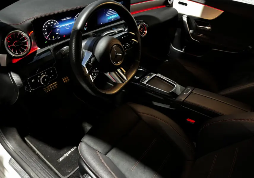Vue intérieure côté conducteur de la Mercedes CLA 250 e AMG Line 2023, sièges noirs et éclairage d'ambiance rouge.