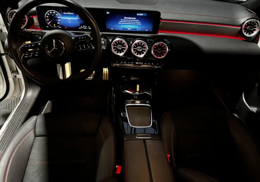 Vue intérieure avant de la Mercedes CLA 250 e AMG Line 2023, tableau de bord noir avec éclairage d’ambiance rouge et écran tactile.