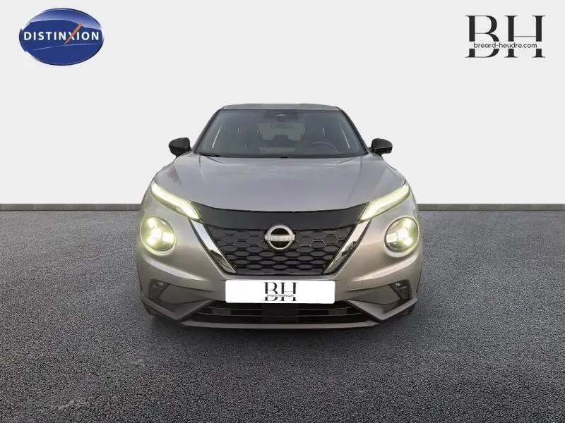 Vue avant du Nissan Juke 1.6 Hybrid 143ch Tekna 2025 en gris perle métallisé avec phares allumés et calandre noire distinctive.