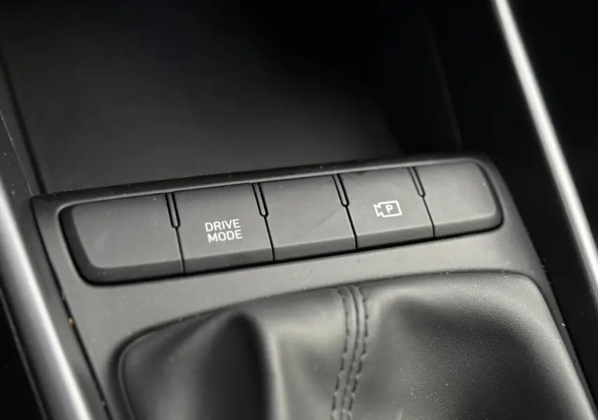 Gros plan sur la console centrale de la Hyundai i20 2025, montrant les boutons Drive Mode et caméra de recul.