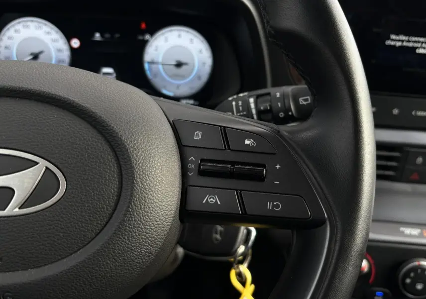Gros plan sur le volant cuir de la Hyundai i20 2025, montrant les commandes au volant côté droit et le tableau de bord numérique.