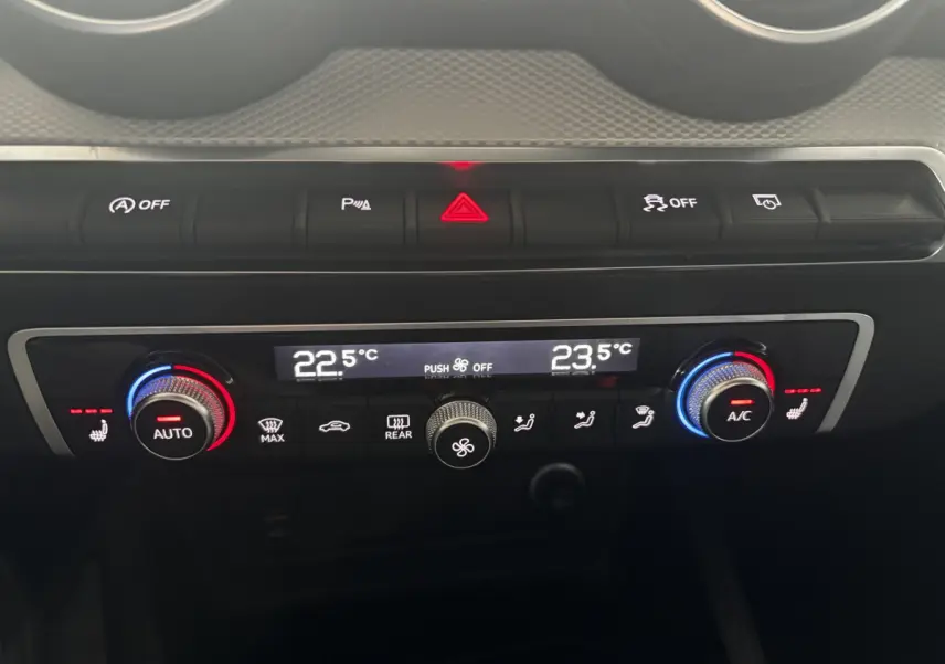 Gros plan sur la console centrale de l’Audi Q2 noire, montrant la climatisation digitale bi-zone avec commandes rotatives et boutons lumineux.