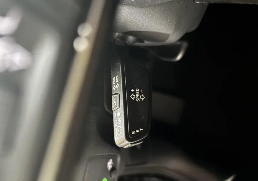 Gros plan sur la commande de régulateur de vitesse au volant d’un Audi Q2 noir, version 35 TFSI S Line.