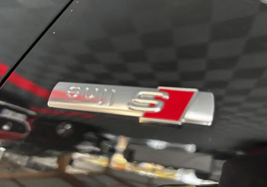 Gros plan sur l’emblème S line argent et rouge sur la carrosserie noire brillante d’un Audi Q2 35 TFSI 2023.