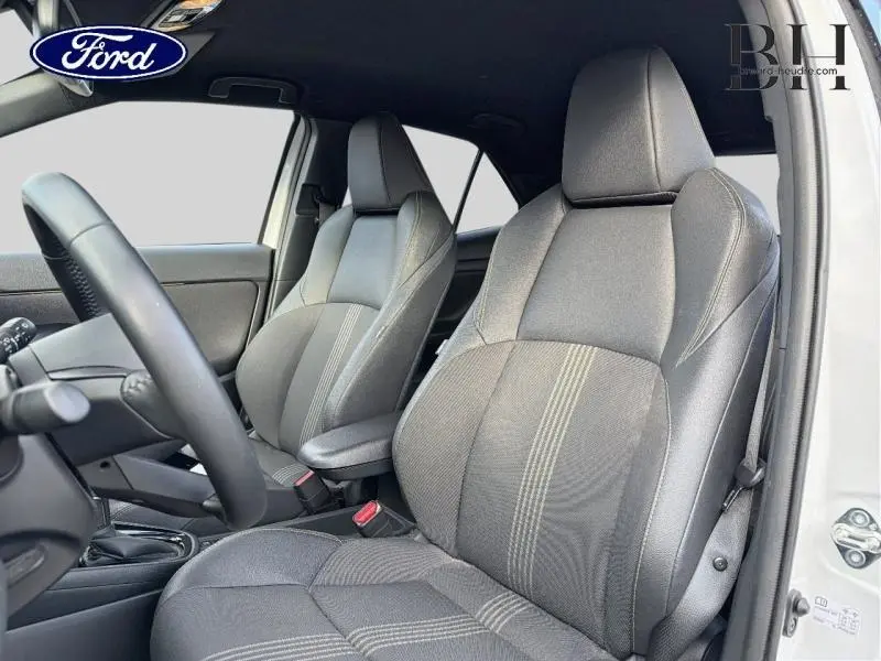 Vue intérieure côté conducteur montrant les sièges tissu gris avec surpiqûres claires et volant multifonction.