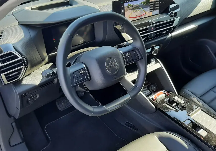 Vue intérieure côté conducteur du tableau de bord et volant noir de la Citroën C4 hybride 2025 avec écran tactile et sellerie cuir.