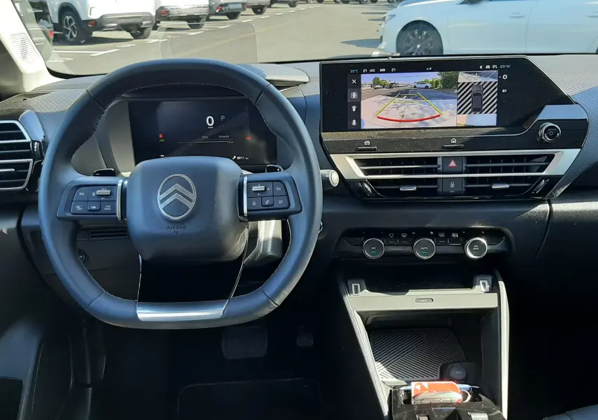 Vue intérieure du poste de conduite du Citroën C4 blanc Okenite 2025, avec tableau de bord numérique et écran central affichant la caméra de recul.