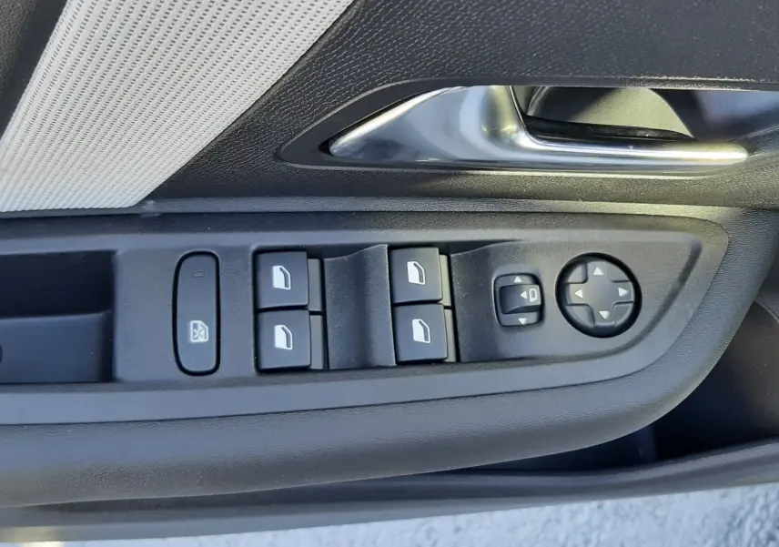 Gros plan sur la commande des vitres et rétroviseurs côté conducteur d'une Citroën C4 blanche, avec poignée intérieure argentée.