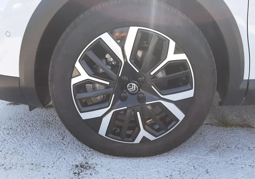 Gros plan sur la roue avant droite d'une Citroën C4 blanche Okenite, mettant en valeur la jante noire et argentée au design géométrique.