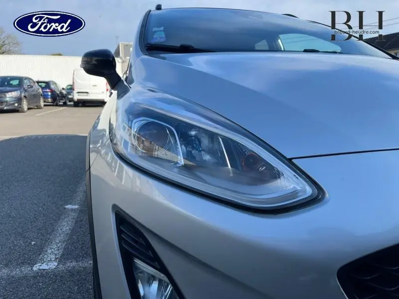 Gros plan sur le phare avant gauche d'une Ford Fiesta 2020 gris lunaire, avec partie du capot et rétroviseur visible.