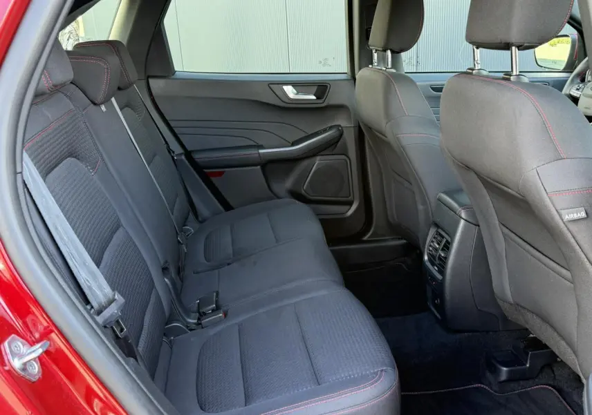 Vue intérieure arrière côté gauche du Ford Kuga rouge Lucifer 2024, sièges tissu noirs avec surpiqûres rouges.