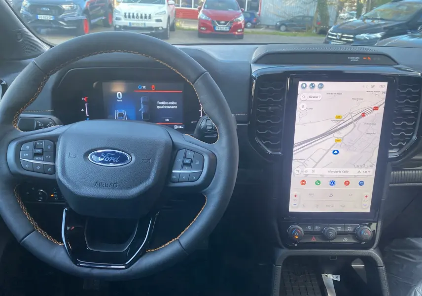 Vue intérieure centrée sur le volant cuir noir avec surpiqûres marron et grand écran tactile vertical du Ford Ranger gris carbone.