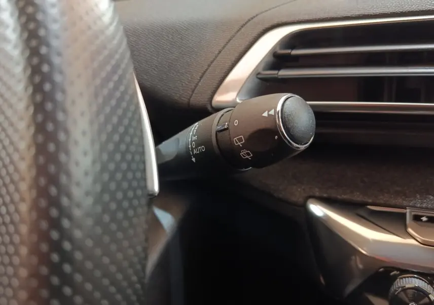 Gros plan sur la commande d’essuie-glace à gauche du volant dans l’habitacle noir du Peugeot 3008 bleu.