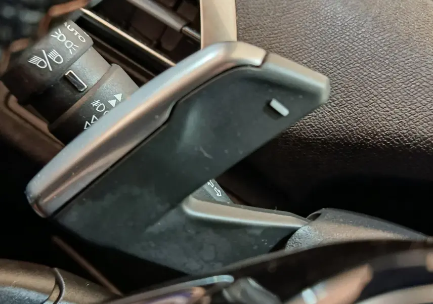 Gros plan sur la palette de changement de vitesse grise et les commandes des phares du Peugeot 3008 hybride bleu.