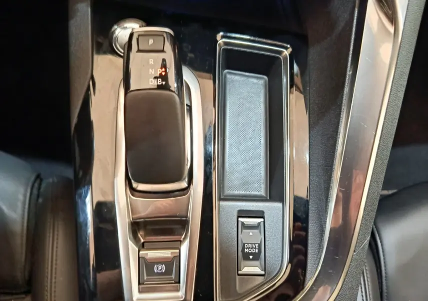 Gros plan sur la console centrale noire brillante du Peugeot 3008 bleu, avec levier de vitesses automatique et bouton Drive Mode.