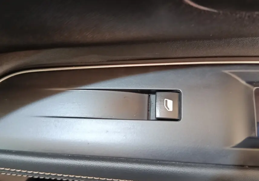 Gros plan sur le bouton de commande de lève-vitre côté conducteur dans l'intérieur noir du Peugeot 3008 hybride bleu.