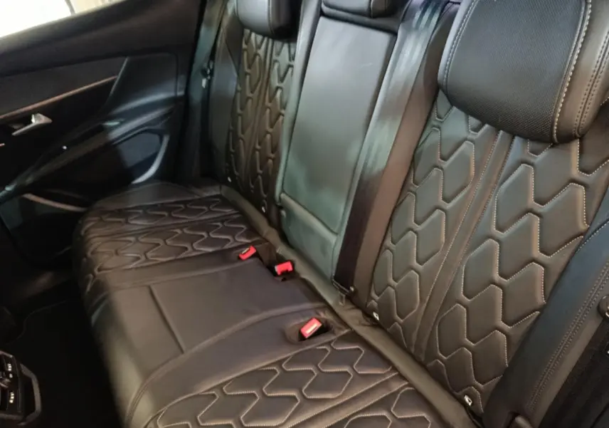 Vue intérieure côté arrière droit montrant la banquette en cuir noir avec surpiqûres hexagonales du Peugeot 3008 Hybrid 225 GT Pack.