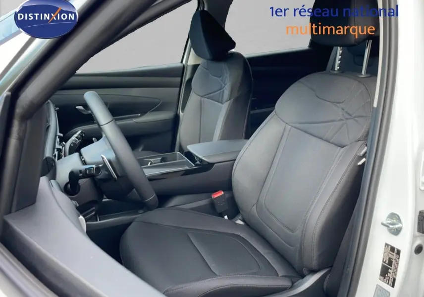 Vue intérieure côté conducteur du Hyundai Tucson 2026 blanc Atlas, sièges tissu noir avec détails couture et volant multifonction.