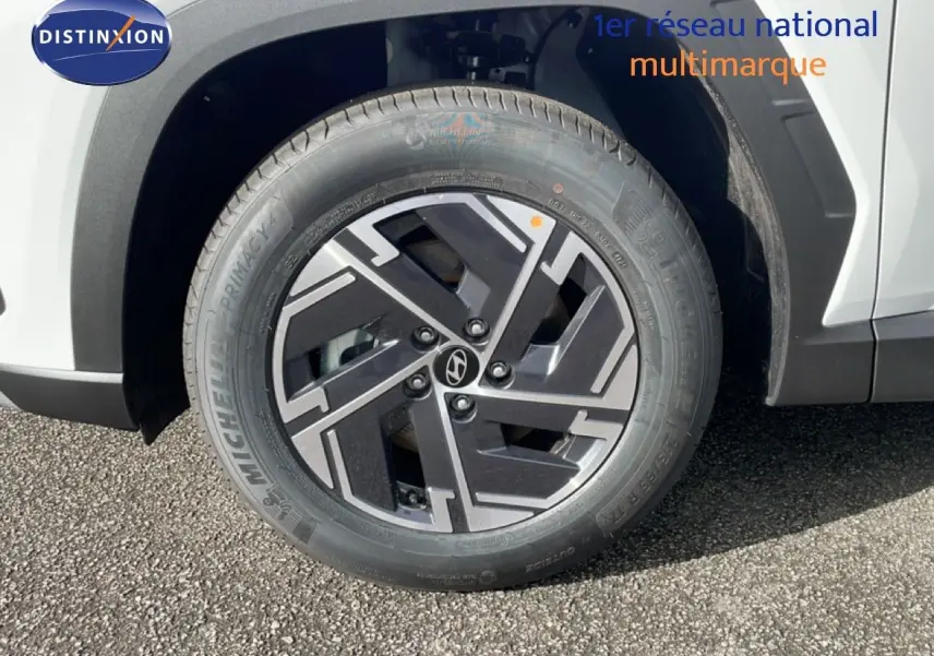 Gros plan sur la roue avant droite du Hyundai Tucson blanc Atlas, mettant en valeur la jante noire et argentée au design moderne.