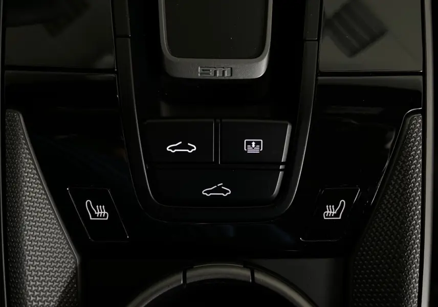 Gros plan sur la console centrale noire brillante de la Porsche 911 argent, avec boutons de toit ouvrant et sièges chauffants.