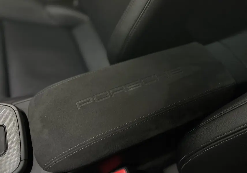 Accoudoir central en alcantara noir avec logo Porsche embossé, entouré de sièges en cuir noir dans une 911 Carrera S.