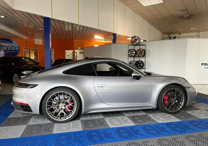 Vue latérale droite d'une Porsche 911 (992) Carrera S argent GT avec jantes RS Spyder et étriers de frein rouges dans un showroom.