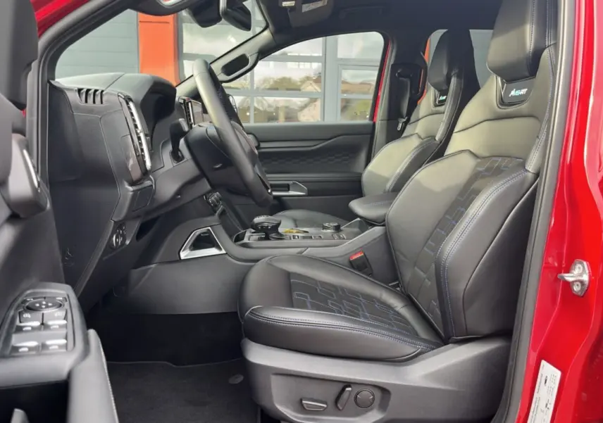 Vue intérieure côté conducteur du Ford Ranger 3.0 V6 240 MS-RT Plus rouge, sièges cuir noirs avec surpiqûres bleues.