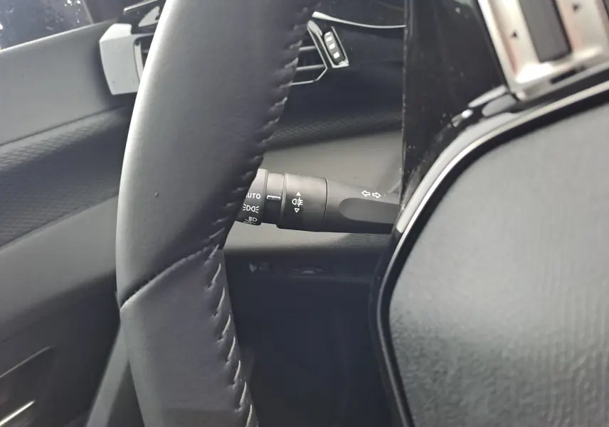 Gros plan sur le volant en cuir noir et la commande des feux à gauche dans l'habitacle d'une Peugeot 308 blanche.