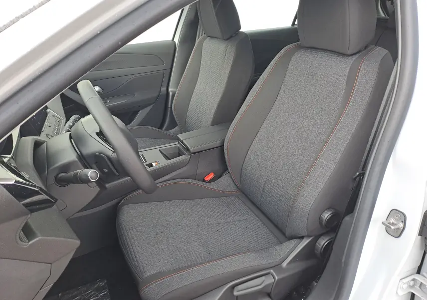 Vue intérieure côté conducteur de la Peugeot 308 2025 blanc Okenite, sièges tissu gris avec surpiqûres orange.